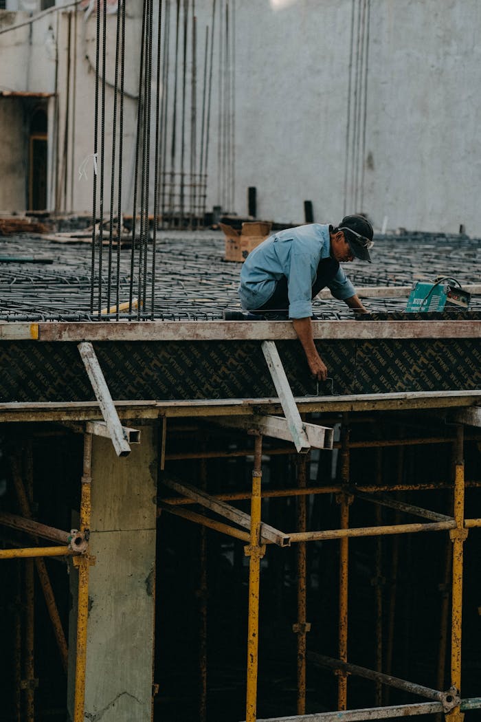 A construction worker is building on a high-rise in an urban setting, focusing on scaffold work.