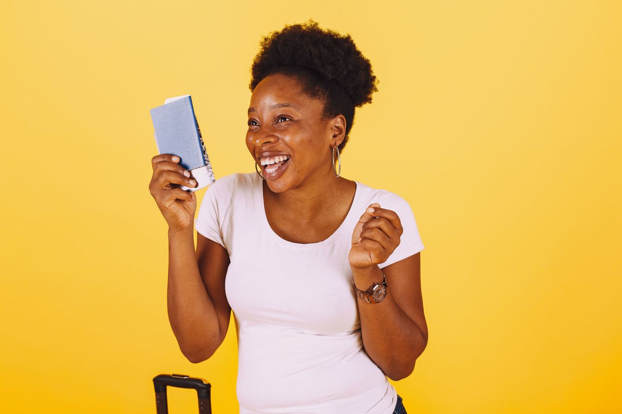 team-03 Smiling woman holding passport ready for a vacation against a yellow background.
